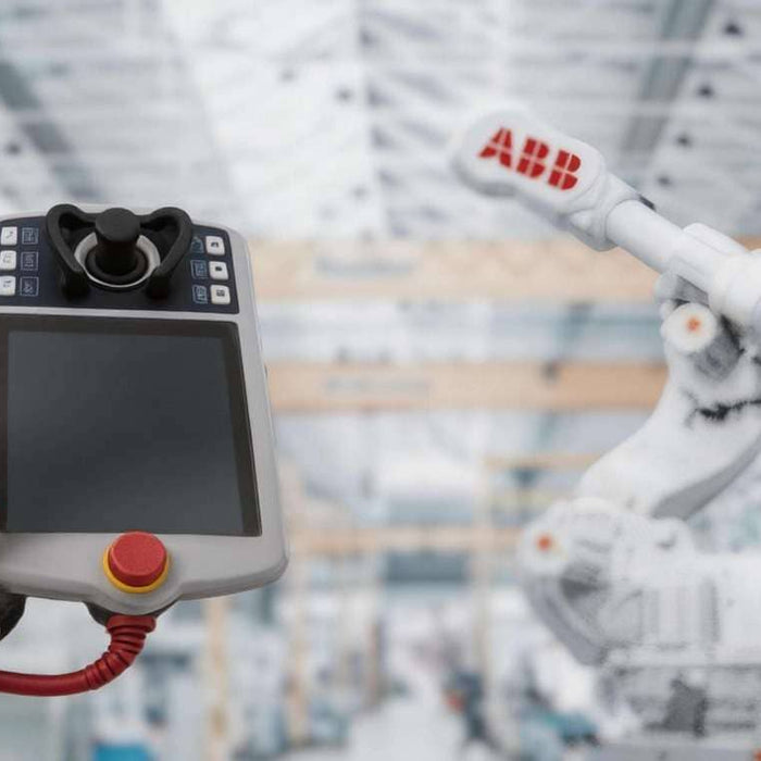 A close-up of an ABB Flexpendant DSQC3120 (3HAC085590-001) held by an operator, highlighting the red emergency stop button against a blurred industrial background with an ABB robot arm.