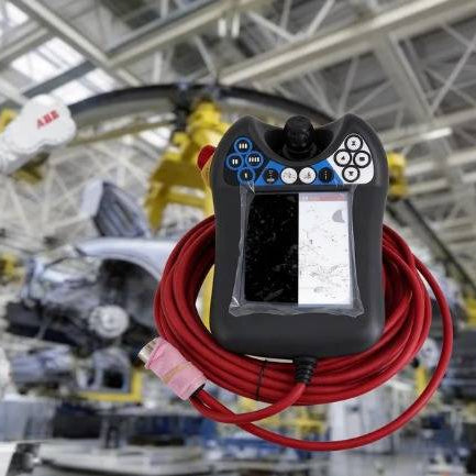 An ABB Flexpendant DSQC679 (3HAC028357-001) with a severely damaged and cracked LCD screen, shown with its red cable in an automotive factory to illustrate physical display failure.