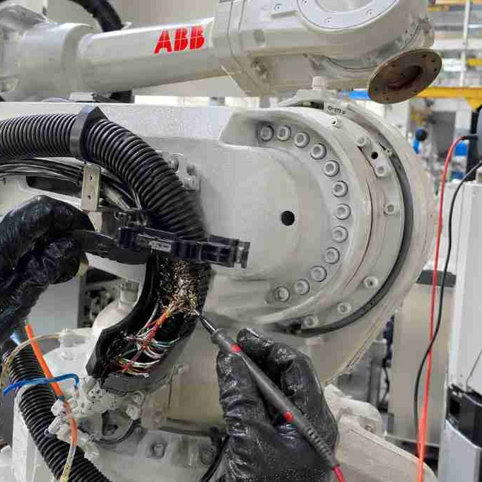 A close-up of a field service technician inspecting a frayed encoder cable inside an ABB robot dresspack to fix an intermittent 39521 SMB communication error.