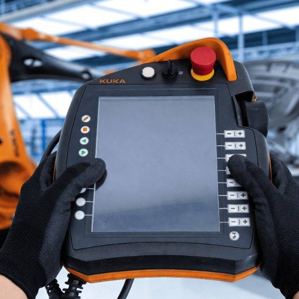An operator holding a KUKA smartPAD KCP4 (00-168-334) in an automotive plant, focusing on the red emergency stop button to illustrate ESC safety chain diagnostics and troubleshooting for KRC4/KRC5 controllers.