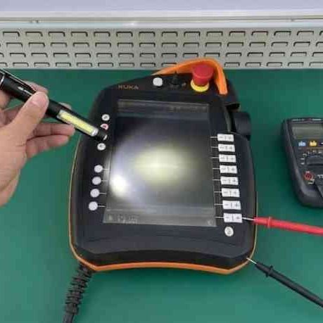 Using a flashlight to diagnose a blank LCD screen on an industrial robot teach pendant, a key step in identifying backlight versus signal failures.