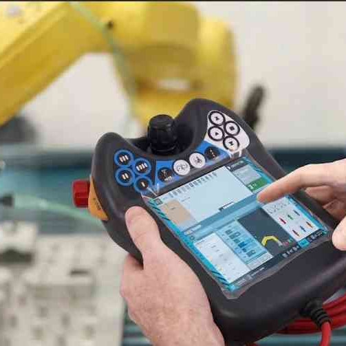 A technician attempting to operate an industrial robot teach pendant with a frozen touchscreen in a production environment.