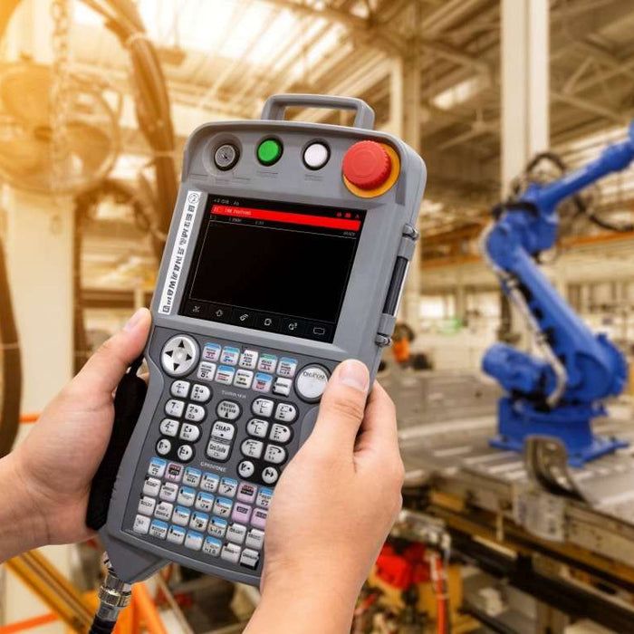 An operator in a high-density automotive production line holding a Yaskawa JZRCR-YPP21-1 DX200 teach pendant with an active alarm list, highlighting the red emergency stop button for troubleshooting safety circuit faults.
