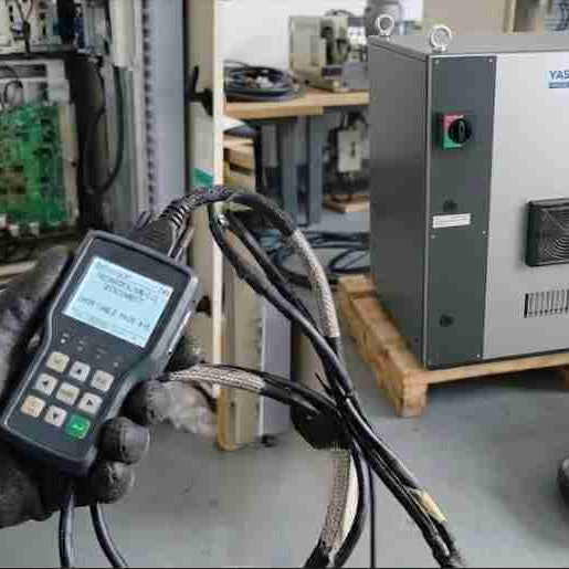 A maintenance engineer diagnosing a Yaskawa robot random disconnect issue inside an open blue YRC1000 controller cabinet, using a diagnostic tool to test high-speed MECHATROLINK communication cables and Sigma-7 servo drive connections.